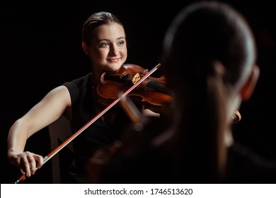 Happy Professional Musicians Playing Classical Music On Violins On Dark Stage