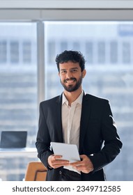Happy professional young latin business man company employee, male corporate manager, businessman office worker looking at camera holding digital tablet standing in office, vertical portrait.