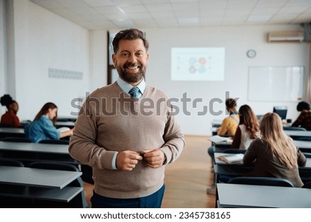 Happy professor in lecture hall at the university looking at camera. His students are int he background.