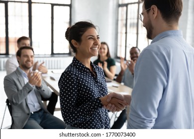 Happy proud excited Indian ethnicity employee get promotion receive praises from boss and cheering and congratulations from diverse staff members shake hands with chief. Recognition of success concept