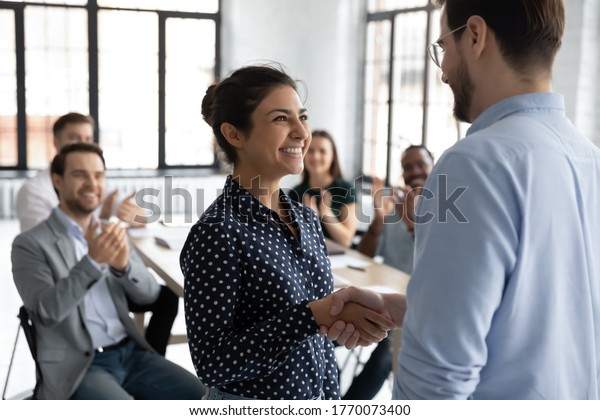 Happy proud excited Indian ethnicity employee get\
promotion receive praises from boss and cheering and\
congratulations from diverse staff members shake hands with chief.\
Recognition of success\
concept