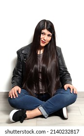 Happy And Proud Latin Young Adult Woman Shows Her Long Straight, Black And Shiny Hair On A White Background With A Leather Jacket And Black Tennis Shoes
