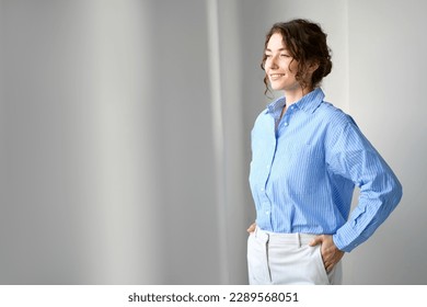 Happy proud young motivated smiling confident professional business woman, happy pretty lady ceo manager leader executive looking at window, thinking, dreaming or future goals standing indoors. - Shutterstock ID 2289568051