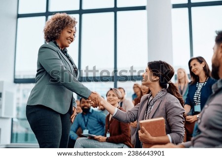 Happy public speaker handshaking with businesswoman from the audience during a seminar in convention center.