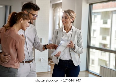 Happy Real Estate Agent Showing To A Couple Plans Of Their New Home. 