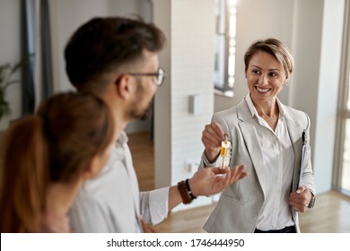 Happy real state agent giving new house key to a young couple.  - Shutterstock ID 1746444950