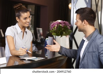 Happy Receptionist And Guest Talking At Hotel Reception.