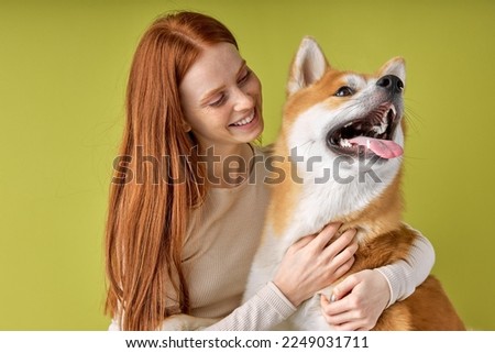 happy Red-haired lady in casual wear hugging purebred pet dog, akita inu dog with owner posing isolated over green studio background. Portrait copy space, for ad. animals, pets concept