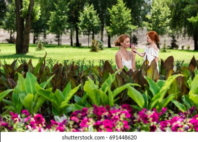 Happy Redhead Mother And Daughter Smelling Flowers Near Flower Bed In Park