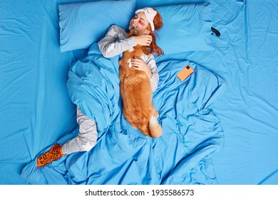 Happy redhead woman embraces dog with love has fun have good relationships with pet stay in bed awake early in morning. Beloved puppy gets hug from female owner. Care obedience friendship concept