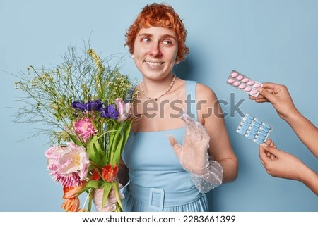 Happy redhead woman refuses to take medicine holds bouquet of flowers suffers from pollen allegry smiles toothily wears dress and jewellery isolated over blue background suffers from runny nose Stock photo © 