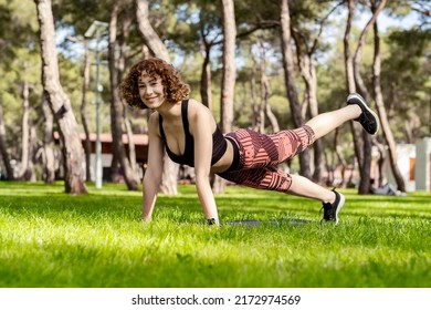 Happy Redhead Woman Wearing Black Sports Bra Standing On City Park, Outdoor Doing Donkey, Kick Exercise, Bird Dog Pose, Working Out, Concept Of Healthy Lifestyle, Yoga.