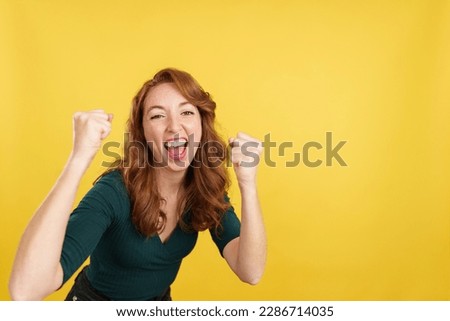 Happy redheaded woman celebrating raising the fists