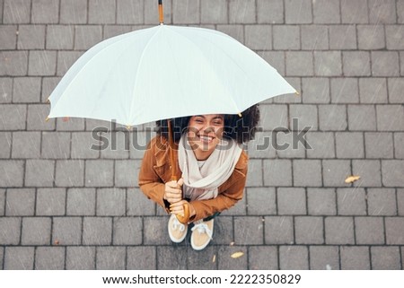 Happy, relax and girl with rain umbrella enjoying outdoor, urban and winter weather with excited smile. Happiness, peace and wellness of black woman with afro standing in rainy city top view.