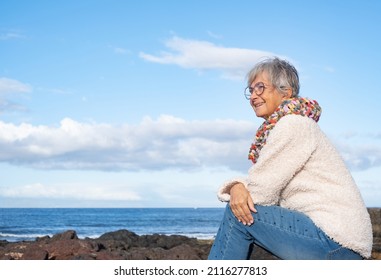 Happy relaxed adult senior woman sitting at the beach wearing sweater and colorful scarf looking away. Smiling elderly gray haired lady enjoying freedom and retirement, horizon over sea. Copy space - Powered by Shutterstock