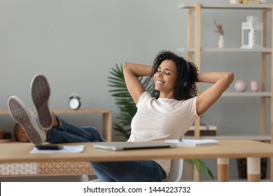 Happy Relaxed African Woman Wear Wireless Headphones Listening To Lounge Music Relaxing After Work Hands Behind Head, Calm Serene Black Girl Student Feel Stress Free Relief Sit At Home Office Desk