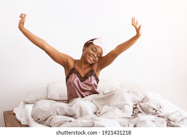 Happy and relaxed after good night sleep. Smiling millennial african american cute woman in mask sits on bed with blanket, stretching after waking up, in bedroom interior, copy space, lens flare - Shutterstock ID 1921431218