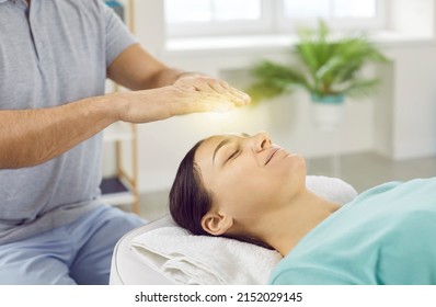 Happy relaxed and calm young woman with closed eyes receiving reiki treatment above head. Male therapist holding hands with yellow glowing light over female client's head lying on massage table. - Powered by Shutterstock