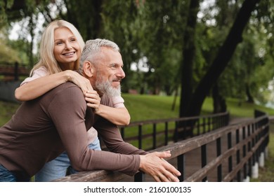 Happy relaxed caucasian mature couple spouses husband and wife hugging embracing together while walking in park on romantic date. - Shutterstock ID 2160100135