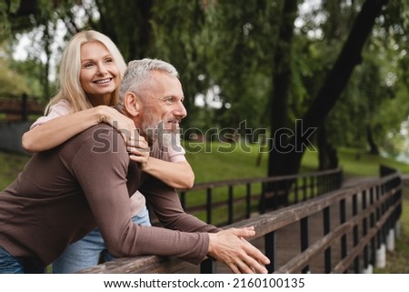 Happy relaxed caucasian mature couple spouses husband and wife hugging embracing together while walking in park on romantic date.