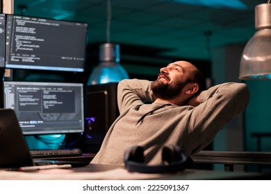 Happy relaxed developer sitting laid back on chair, feeling pleased about software development work in office. Enjoying server programming success late at night, server code html script.