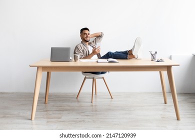 Happy Relaxed Man Typing Message Sms On Cell, Resting Legs On Table During Remote Work From Home Office, Smiling Male Freelancer Looking At Phone Screen, Chatting Online At Workplace, Full Body Length