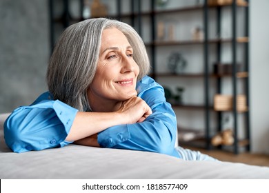 Happy Relaxed Mature Old Woman Resting Dreaming Sitting On Couch At Home. Smiling Mid Aged Woman Relaxing. Peaceful Serene Grey-haired Lady Feeling Peace Of Mind Enjoying Lounge On Sofa And Thinking.