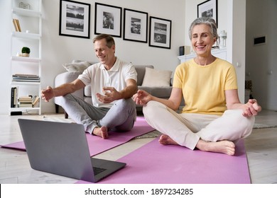 Happy relaxed old 60s couple having fun meditating together at home with laptop. Fit healthy senior mid aged man and woman laughing doing yoga exercise watching online class, feeling no stress free.