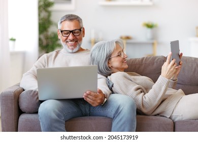 Happy relaxed old retired family couple using modern technologies laptop and digital tablet while relaxing resting on sofa in living room, senior man and woman surfing internet in free time - Powered by Shutterstock