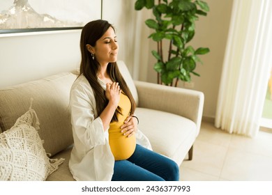 Happy relaxed pregnant woman smiling while doing breathing exercises and relaxing while thinking about a meditation at home - Powered by Shutterstock