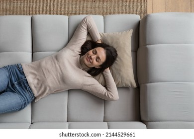 Happy relaxed pretty young woman lying on sofa at home, daydreaming, thinking over good future plans, breathing fresh air, enjoying leisure time, pause, laziness, reloading. Top view