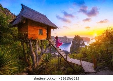 Happy and relaxed travel woman watching sunrise, tree house with diamond beach, Atuh beach in Nusa Penida island, Bali, Indonesia.