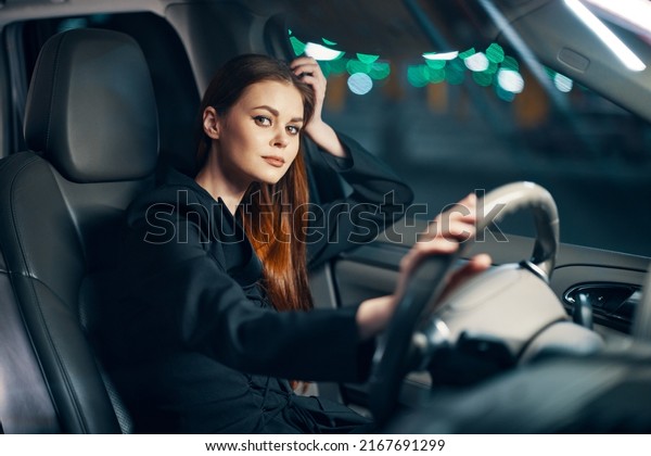 a\
happy, relaxed woman enjoys a night drive while sitting in a car\
and holding her hand near her head in a relaxed\
pose