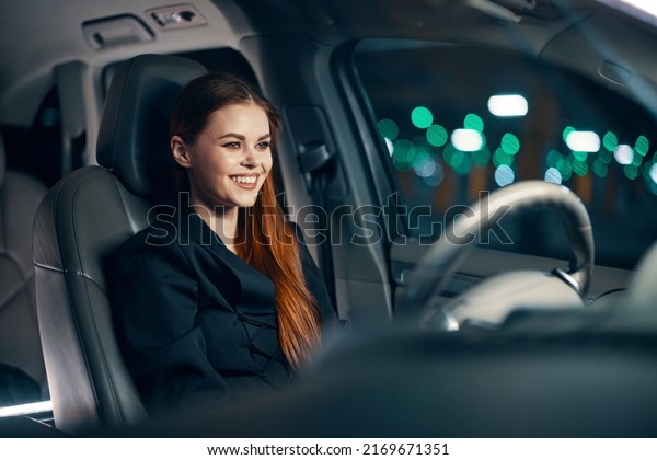 a happy, relaxed woman enjoys a night drive while\
sitting in a car