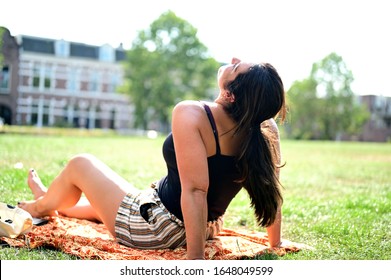 Happy And Relaxed Woman Sunbathing A Bit In A Nice Green Park In A Suburban Area In Amsterdam, The Netherlands