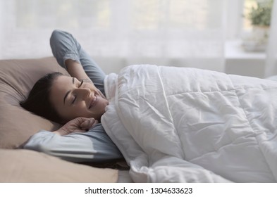Happy relaxed woman waking up early in the morning and stretching her arms, healthy lifestyle concept