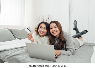 Happy Relaxed Young Female Friends Doing Online Shopping Through Laptop And Credit Card At Home