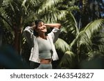 Happy relaxed young Hispanic woman enjoying summer sunny day with eyes closed feeling no stress, peace of mind, mental balance relaxing standing in green nature park among tropical trees.