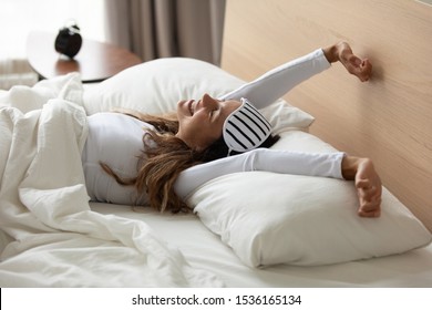Happy relaxed young woman with sleeping mask awaken in cozy bedroom, stretching hands, feeling energetic. Smiling millennial mixed race girl enjoying lazy weekend morning in comfortable bed at home. - Shutterstock ID 1536165134