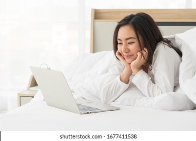 Happy, Relaxing Young Beautiful Asian Female Watching Movie Or Series On Notebook In Emotional Smile Happily While Chin On Hand And Laying On The Bed In Her Bedroom. Chill Out And Leisure Concept.