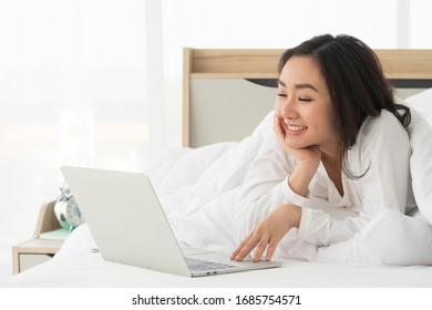 Happy, Relaxing Young Beautiful Asian Female Watching Movie Or Series On Notebook In Emotional Smile Happily While Chin On Hand And Laying On The Bed. Day Off, Chill Out And Leisure Concept.