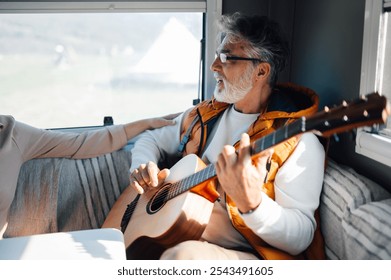 Happy retired couple embraces van life, strumming a guitar and singing in their cozy camper van on a scenic road trip, radiating joy and love - Powered by Shutterstock