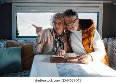 Happy retired couple reading a book together while traveling in their camper van, enjoying their free time and the beautiful view outside - Powered by Shutterstock