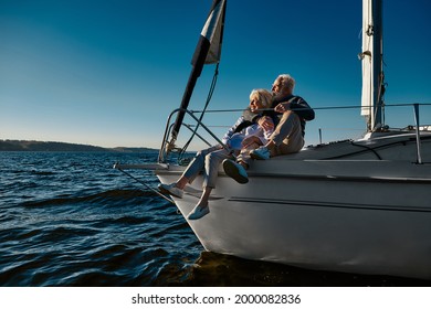 Happy retired family couple relaxing on a sail boat or yacht deck floating in a calm blue sea, hugging and enjoying amazing view