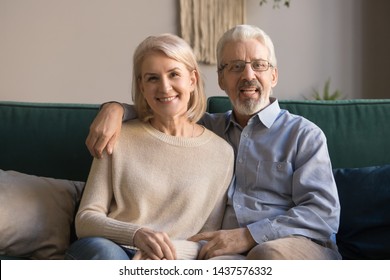 Happy Retired Old Family Couple Looking At Camera Recording Vlog, Smiling Senior Spouses Embracing Doing Distance Video Chat Call Talking To Webcam Sitting On Sofa At Home, Webcamera View, Portrait