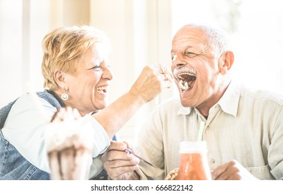 Happy retired senior couple in love enjoying bio icecream cup - Joyful elderly lifestyle concept - Wife feeding husband and having fun at bar cafe restaurant during evergreen vacation - Retro filter - Powered by Shutterstock