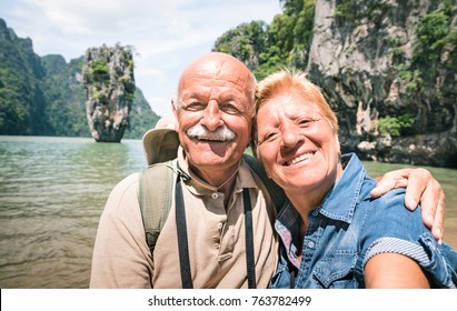 Happy Retired Senior Couple Taking Travel Selfie Around World - Active Elderly Concept With People Having Fun Together At James Bond Island In Thailand - Mature People Lifestyle - Warm Day Filter