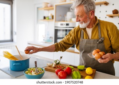 Happy Retired Senior Man Cooking In Kitchen. Retirement, Hobby People Concept