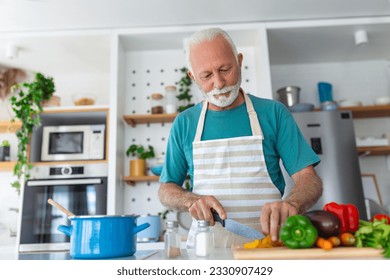 Happy retired senior man cooking in kitchen. Retirement, hobby people concept. Portrait of smiling senior man cutting vegetables - Powered by Shutterstock