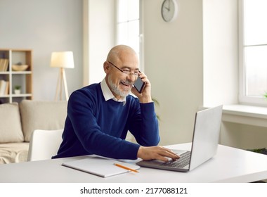 Happy retired senior man talking on his mobile phone. Cheerful bald man in glasses sitting at his working table, speaking to a friend on his cellphone and using his laptop at the same time - Powered by Shutterstock